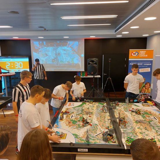 Eine Gruppe junger Jungen spielt mit Legosteinen auf einem großen Tisch. Sie arbeiten an der Errichtung einer Lego-Stadt.