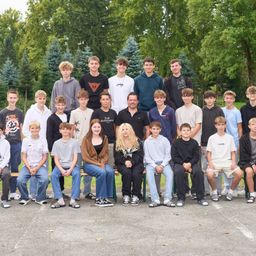 Eine Gruppe von Schülern und zwei Frauen posiert für ein Foto im Freien, mit Bäumen im Hintergrund.