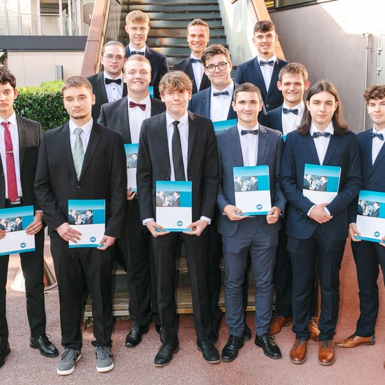 Eine Gruppe junger Männer in Anzügen und Fliegen, die auf einer Treppe stehen und ein Heft halten, wahrscheinlich für ein Foto posend.