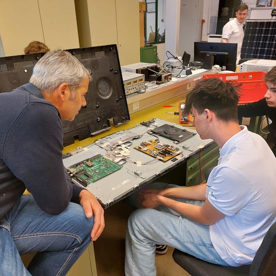 Ein Mann inspiziert einen zerlegten Computer, während ein anderer an einer Schaltung in einem Labor arbeitet.