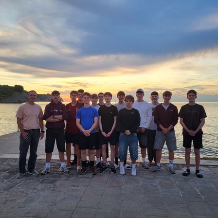 Eine Gruppe junger Männer posiert für ein Foto auf einem Pier, mit Meer und Sonnenuntergang im Hintergrund.