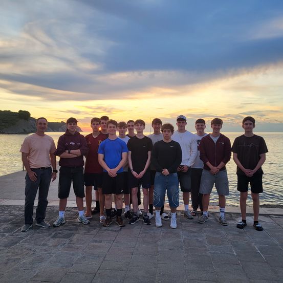 Eine Gruppe junger Männer posiert für ein Foto auf einem Pier, mit Meer und Sonnenuntergang im Hintergrund.