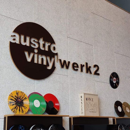 Eine Wand mit dem Schild 'austro vinyl werk2'. Darunter sind verschiedene Schallplatten und ein Buch mit dem Titel 'Mance' ausgestellt.