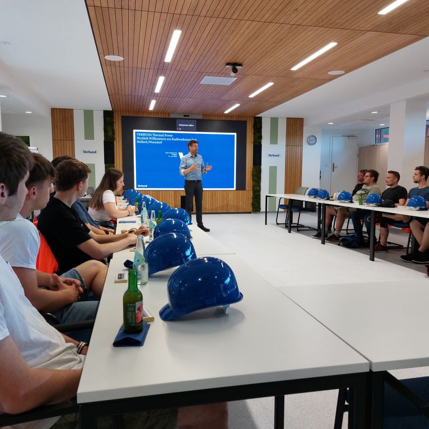 Ein Klassenzimmer mit mehreren Schülern, die vor einem Mann sitzen, der vor einer großen Leinwand eine Präsentation hält.