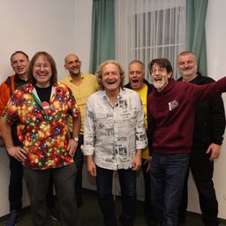 Eine Gruppe von Männern steht zusammen und lächelt für ein Foto. Einer trägt ein Shirt mit gedruckten Designs.