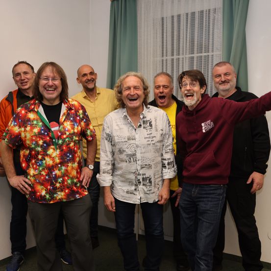 Eine Gruppe von Männern steht zusammen und lächelt für ein Foto. Einer trägt ein Shirt mit gedruckten Designs.