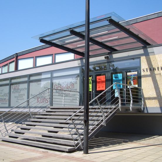 Das Äußere eines modernen Gebäudes mit Glastüren und einer Treppe, die verschiedene Poster und Werbung zeigt.