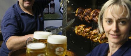 Zwei Personen in blauen Hemden servieren Bier und Drehspießhähnchen in einem Restaurant.