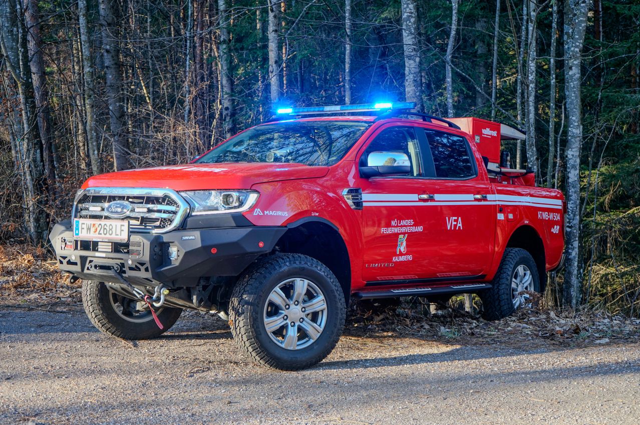 Ein roter Ford Ranger Pickup-Truck mit blinkenden Lichtern auf dem Dach steht auf einer Kiesstraße. Das Kennzeichen lautet '8LF'. Hinter ihm stehen Bäume.