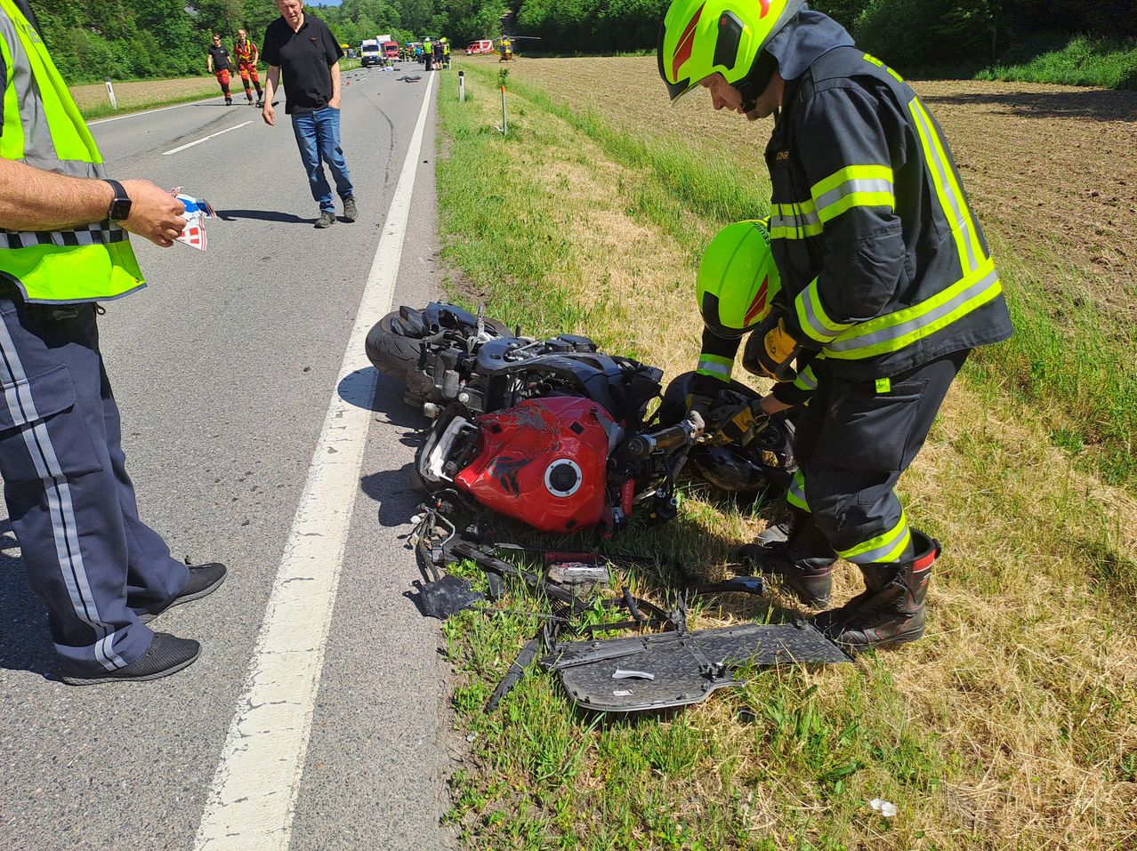 Feuerwehrleute kümmern sich an der Straßenseite um einen Motorradunfall mit beschädigten Geräten und Trümmern.