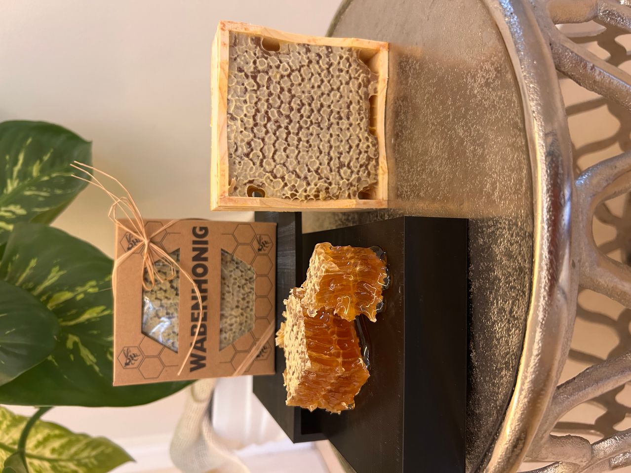 A wooden box with a honeycomb inside and a small piece of honeycomb on a black surface.