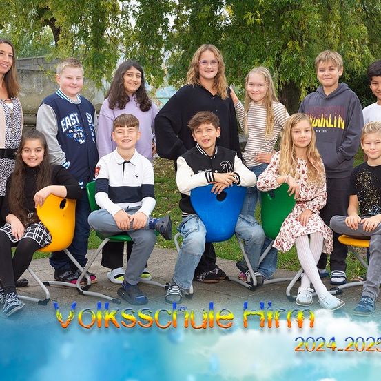 Eine Gruppe von Schülern der Volksschule Himm posiert für ein Foto. Das Bild zeigt ihre Lächeln und den Hintergrund mit Bäumen und einer bewölkten Himmel. Der Textüberlagerung steht 'Volksschule Himm 2024-2025'.