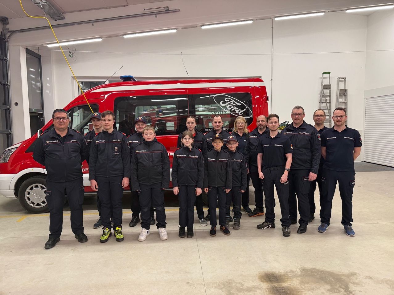 Eine Gruppe Feuerwehrleute und junge Menschen posieren für ein Foto vor einem roten Ford-Fahrzeug.