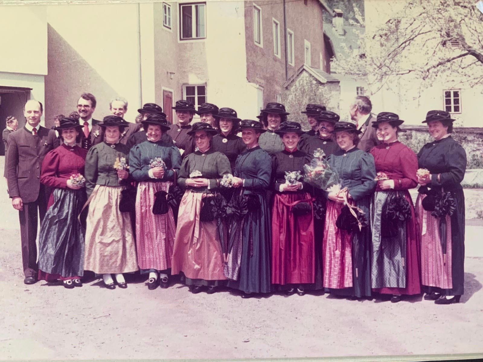 Eine Gruppe von Menschen in Vintage-Kleidung posiert für ein Foto vor einem Gebäude mit Bäumen im Hintergrund.