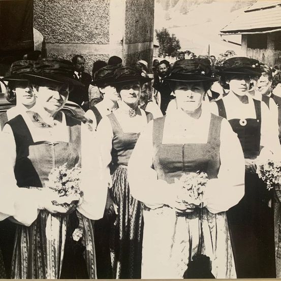 Eine Gruppe von Frauen in traditioneller Kleidung, Hüten und mit Blumen, die für ein Foto zusammenstehen.