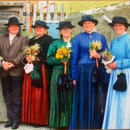 Eine Gruppe von Menschen in traditioneller Kleidung und Hüten, einer hält einen Korb und andere halten Blumensträuße.