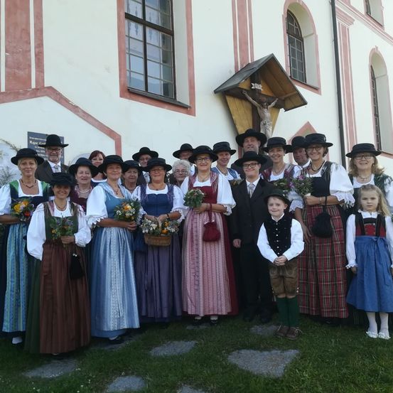 Eine Gruppe von Erwachsenen und Kindern in traditioneller Kleidung, die für ein Foto vor einem Gebäude posiert.