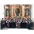 Eine Gruppe von Menschen in traditioneller Kleidung steht vor einem kunstvollen Altar in einer Kirche.