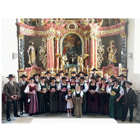 Eine Gruppe von Menschen in traditioneller Kleidung steht vor einem kunstvollen Altar in einer Kirche.