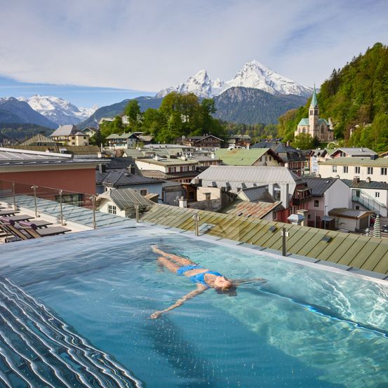 Eine Frau schwimmt in einem Pool auf dem Dach mit Blick auf eine Stadt in den Alpen.