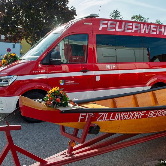 Ein roter Feuerwehrwagen ist auf einer Straße geparkt und zieht ein gelbes Boot mit Blumen darauf.