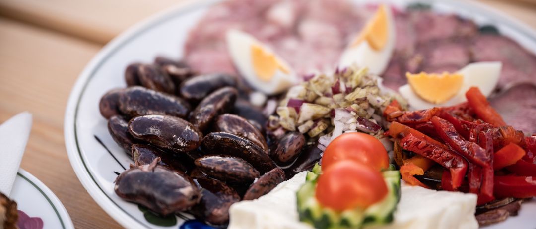 Ein weißer Teller mit verschiedenen Lebensmitteln wie Bohnen, Eiern, Fleisch und Gemüse auf einem Holztisch.
