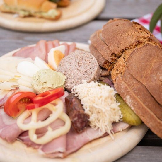 Ein Holzteller mit einer Auswahl an Lebensmitteln, darunter geschnittenes Fleisch, Käse, Eier, Gurken und Brot.