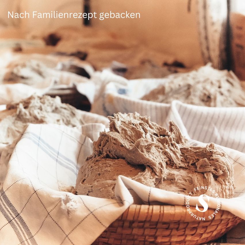 Ein Korb mit Teig, bedeckt mit einem Tuch, auf einer Holzoberfläche platziert. Der Teig hat die Form einer Kugel. Er ist wahrscheinlich bereit zum Backen.
