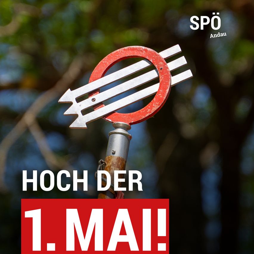 Ein roter Schild mit weißen Pfeilen, die eine Rechtskurve anzeigen, steht für Hoch der 1. Mai. Der Hintergrund ist unscharf mit grünen Bäumen.