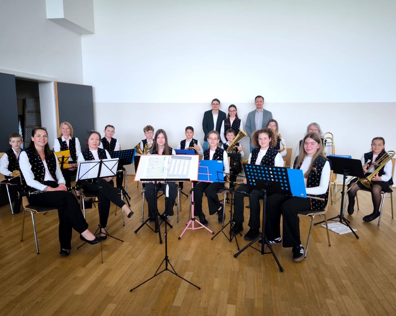 Eine Gruppe junger Musiker, darunter Posaunisten, sitzt in einem Raum mit Notenständern und Noten, möglicherweise in Vorbereitung auf eine Aufführung.