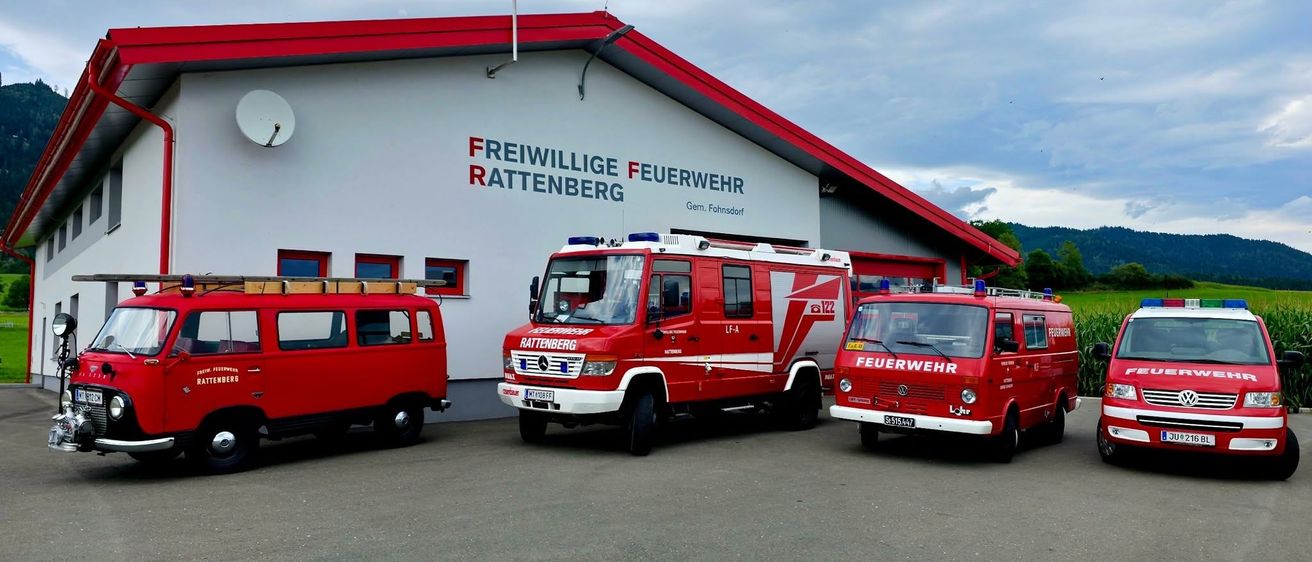 Vier rote Feuerwehrfahrzeuge sind vor einem weiß gestrichenen Gebäude mit rotem Rand geparkt. Das Gebäude trägt die Aufschrift Freiwillige Feuerwehr Rattenberg.