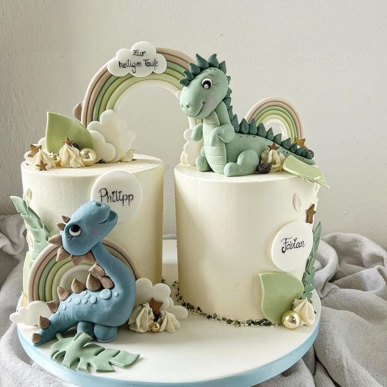 Zweistufiger Kuchen mit zwei Drachen, einem grünen und einem blauen, obenauf. Der Kuchen hat Wolken, Sterne und einen Regenbogenbogen. Die Namen 'Philipp' und 'Fabian' sind auf dem Kuchen eingraviert.