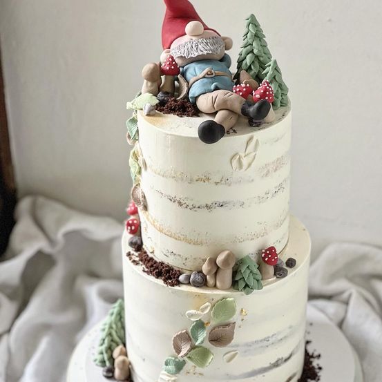 Ein dreischichtiger Kuchen, dekoriert mit weißer Glasur und essbaren Elementen wie Pilzen und Blättern. Eine Zwergfigur ruht auf der obersten Schicht.