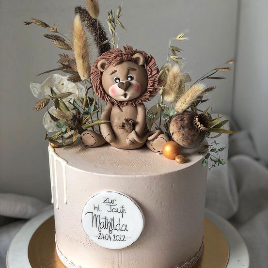 Ein Kuchen mit einer braunen Löwenfigur darauf, umgeben von Blumen und Blättern. Der Kuchen trägt die Aufschrift 'Zur Taufe Matilda 24.04.2022'.