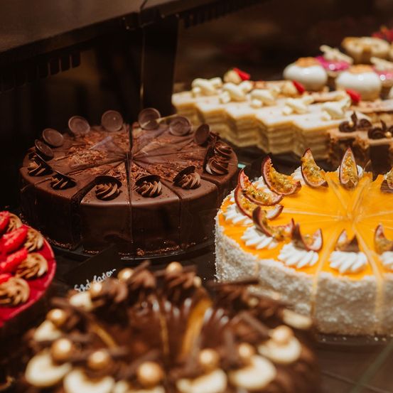 Eine Ausstellung verschiedener Kuchen mit Schokoladen-, Obst- und Sahnetoppings in einem Bäckereiladen.