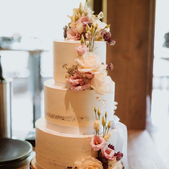 Ein vierstöckiger Hochzeitskuchen mit rustikalem Thema, der mit weißer Glasur und Blumendekorationen auf jeder Etage versehen ist.