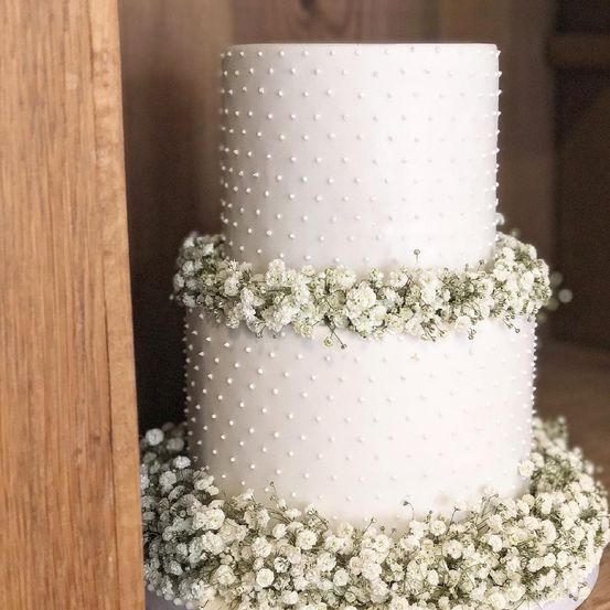 Ein dreistöckiger weißer Kuchen mit winzigen weißen Punkten und weißen Babys-Atem-Blumen um die Etagen.