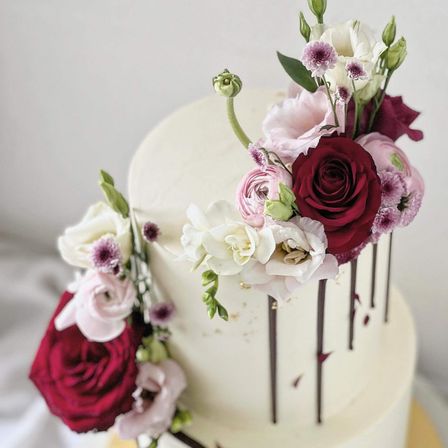 Eine weiße Hochzeitstorte mit dunkelroten und rosa Blumen oben. Der Kuchen hat drei Schichten mit dunkelroten Glasuren und weißen Blumen.