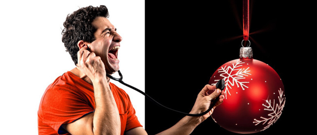 A man is screaming while holding a stethoscope to a red Christmas ornament with a snowflake pattern.