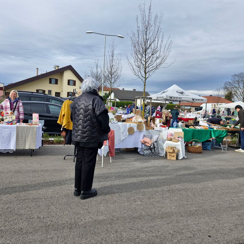 A person stands near a flea market on a cloudy day, with various stalls and items displayed under tents.