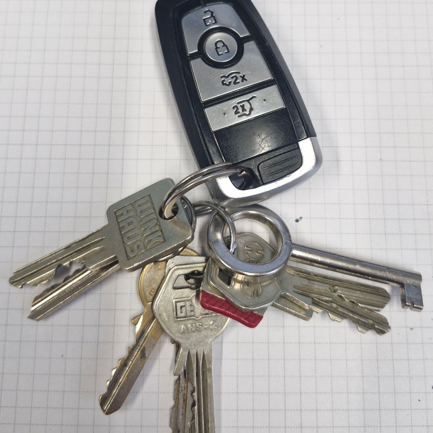 Ein Satz Autoschlüssel mit einem Schlüsselanhänger und einem roten Schlüssel, auf einem Rasterhintergrund dargestellt. Der Schlüsselanhänger hat silberne Knöpfe und das Wort 'MINI' darauf.