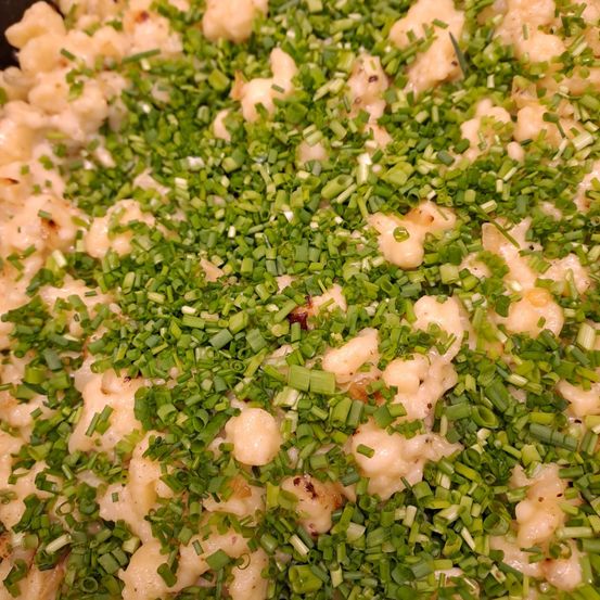 Eine Nahaufnahme eines cremigen Gerichts, das mit grünen Schnittlauch bestreut ist. Es handelt sich wahrscheinlich um einen Makkaroni-Käse mit cremiger Konsistenz, der mit gehackten Frühlingszwiebeln garniert ist.