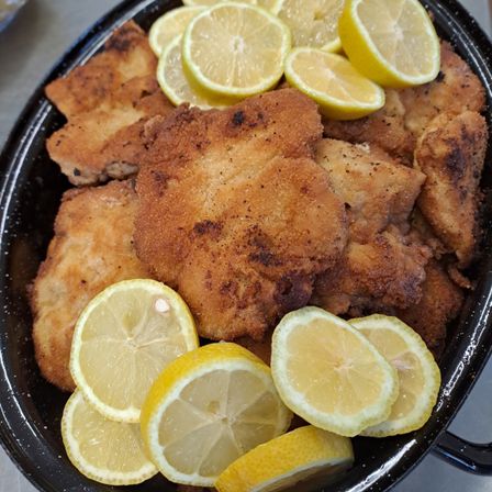 Ein schwarzes Gericht gefüllt mit knusprigem gebratenem Hähnchen, paniert und mit Gewürzen bestreut, begleitet von mehreren Zitronenscheiben.