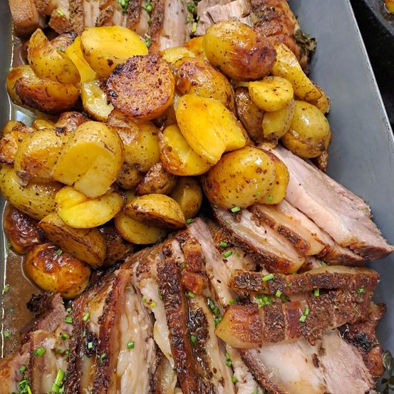 Eine Platte mit gebratenen Kartoffeln und geschnittenem Schweinebauch. Die Kartoffeln sind goldbraun und knusprig, mit Kräutern garniert. Der Schweinebauch ist zart, saftig und leicht angekohlt.