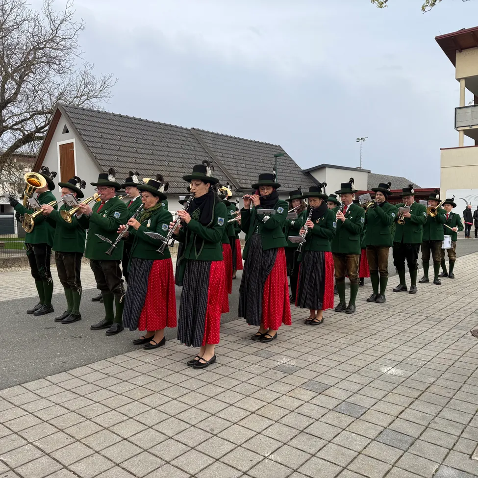 Eine Musikkapelle in Grün und Rot spielt Instrumente auf einer gepflasterten Straße vor einem Haus.