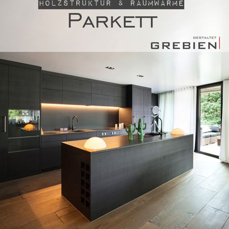 Eine moderne Küche mit schwarzen Schränken und Holzböden, mit einer zentralen Insel mit Lampe und Kakteen. Es gibt ein Waschbecken mit Wasserhahn, ein Fenster mit Vorhängen und eine Schiebetür, die zu einer Terrasse führt.