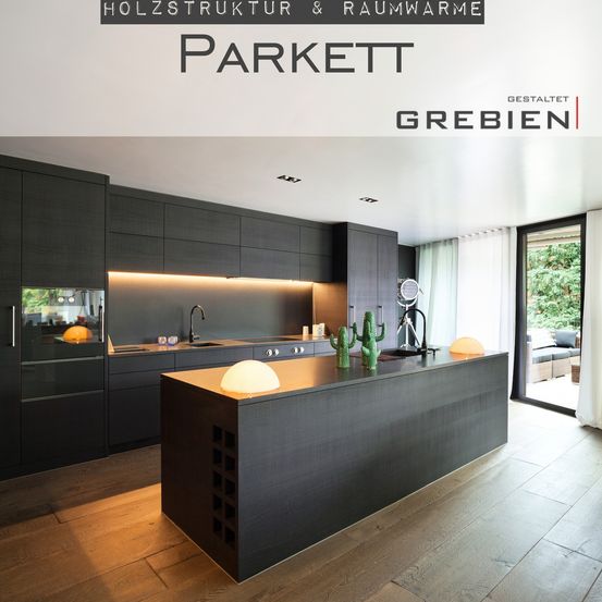 Eine moderne Küche mit schwarzen Schränken und Holzböden, mit einer zentralen Insel mit Lampe und Kakteen. Es gibt ein Waschbecken mit Wasserhahn, ein Fenster mit Vorhängen und eine Schiebetür, die zu einer Terrasse führt.