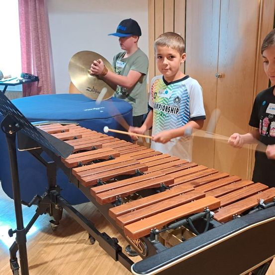 Drei Jungen spielen in einem Raum Musikinstrumente. Ein Junge spielt das Xylophon, während die anderen beiden die Trommeln spielen.