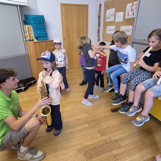 Eine Gruppe von Kindern übt in einem Raum mit ihren Instrumenten Musik. Ein Junge spielt Saxophon, während andere die Blockflöte spielen.