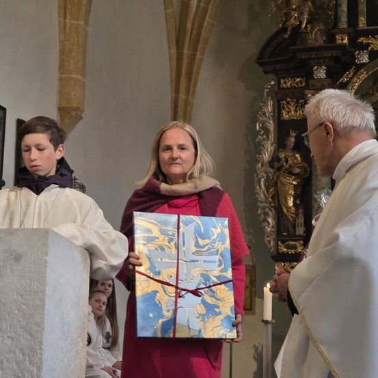 Ein Priester und eine Frau mit einem großen Geschenk stehen neben einer Kanzel in einer Kirche.